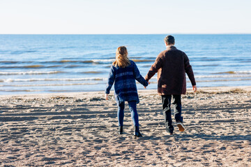 Loving couple walks on beach along sea on sunny autumn day. Weekend and lifestyle concept. Back view. High quality photo