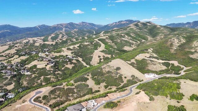 Drone view of mountain roads and scattered homes across dry and green ridges near Bountiful