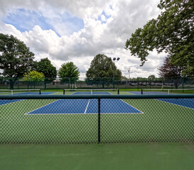 Fototapeta premium Outdoor Pickleball Courts. New empty pickle ball courts located within a public park. Summer scene with cloudy blue skies. View looking over a dividing fence between the courts.