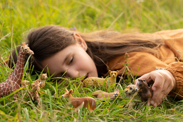 girl in the grass with toy animals. child studying the surrounding nature. game for studying animals
