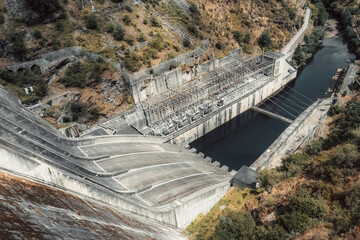 Wide-angle view of a massive concrete dam with curved spillways and an electrical substation at its...
