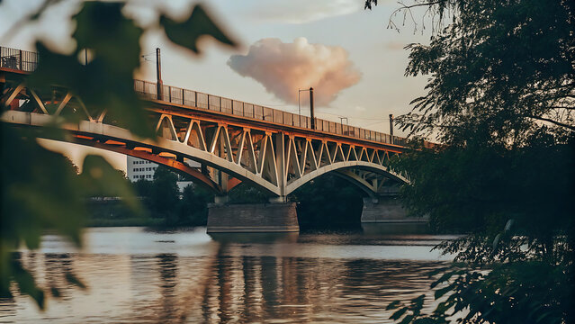 A bridge arches over a calm river, framed by trees and a soft sunset sky.
