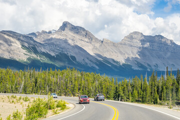 Fototapeta premium Car driving along Icefields Parkway toward towering Rocky Mountains