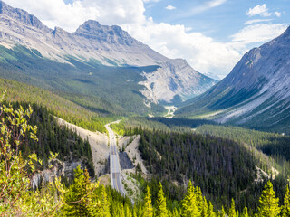 Car driving along Icefields Parkway toward towering Rocky Mountains
