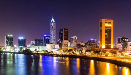 Obraz premium City skyline at night with illuminated buildings reflecting in the water.