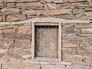 Rustic stone wall with a wooden window frame and wire grid detail