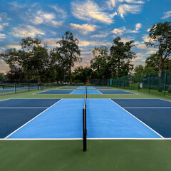 Outdoor Pickleball Courts. Side view of pickle ball courts, looking across the nets of several courts in a row. Public city park setting with cloudy blue Summer sky.