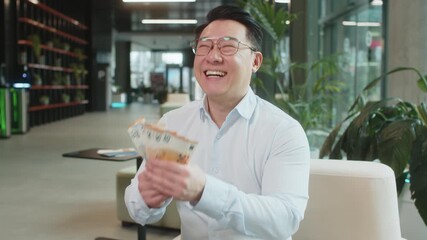 Happy mature businessman in formal shirt counting cash money euro banknotes and looking up, celebrate, success career, income, wealth at modern office lobby. Confident smile employee in eyeglasses. - Powered by Adobe