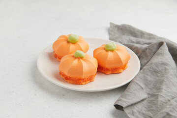 Three orange pumpkin shaped desserts with green tops, placed on a white plate with a gray cloth...