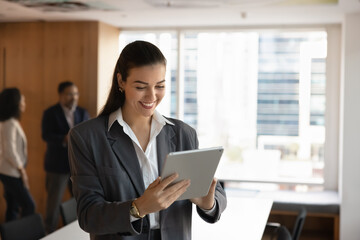 Staying productive on the go. Smiling young female business leader executive using tablet standing in open office browse digital presentation before meeting confirm appointment send email. Copy space