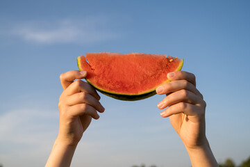 Juicy red watermelon slice in hand, on sunset park background