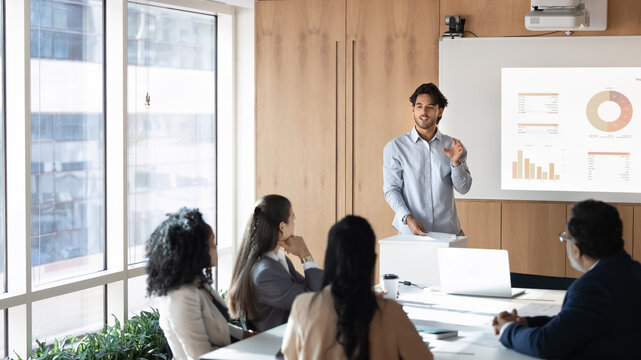 Whiteboard presentation in digital age. Young businessman multiethnic team leader teacher trainer share knowledge on boardroom meeting presenting idea pitch for project startup at workplace conference