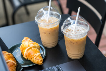 Take away coffee in a plastic cup and fresh croissant, black table.