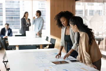 Joint project. Two diverse young businesswomen collaborate on financial planning data analysis...