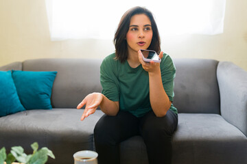 Cute Hispanic woman working from home using smartphone and recording a voice note