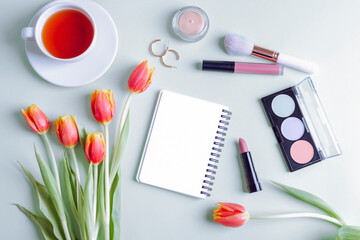 Blank notepad, cup of tea, makeup cosmetics and bouquet of red tulips on light background, top view. Women's day or Mother's day concept. Flat lay, mockup