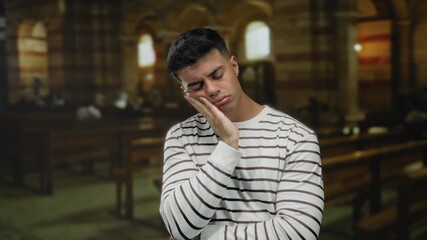 Young man wearing striped shirt in church with thoughtful expression in contemplative indoor setting showcasing serene ambiance.