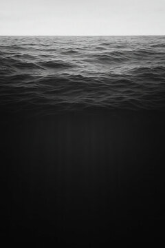 Black and white vertical cutaway of the ocean: textured wave surface above and a deep, dark water column below, atmospheric and moody with generous copy space.