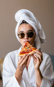 Woman in bathrobe with towel wrap, home morning setting, eating pizza slice, unposed relaxed mood