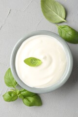 Tasty yoghurt with basil in bowl on light grey table, flat lay