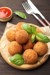 Delicious fried croquette balls with basil on wooden table, closeup