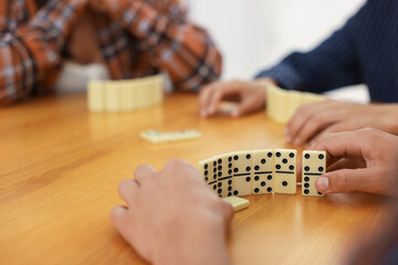 friends playing dominoes at wooden table against light background, closeup