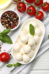 Tasty mozzarella cheese, tomatoes, basil and spices on white wooden table, flat lay