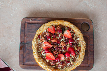 Imagen cenital de una pizza de fresas con frutos secos sobre una tabla de madera