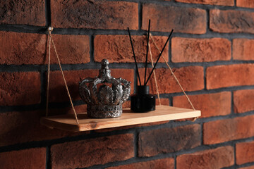 Wooden shelf with reed diffuser and home decor on brick wall