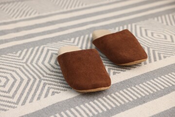 Stylish brown slippers on carpet with pattern, closeup