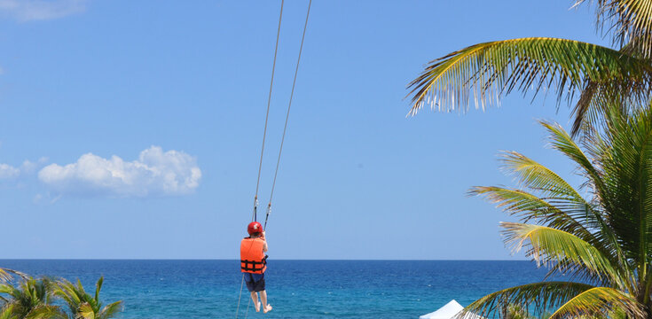 Boy on zipline in paradise on vacation with blue sky and palm trees