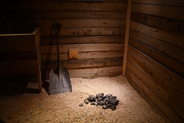 Horse stall. Pile of manure on hay. Shovel leaned against wall. Dim lighting. Newer building.