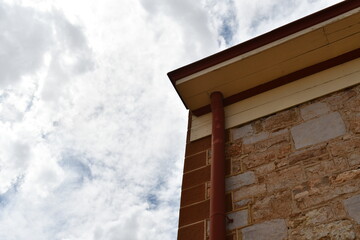 Corner of stone building. Gutter downspout. Cloudy sky.
