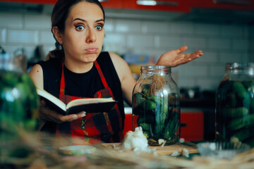 Puzzled Housewife Holding her Recipe Book with Pickling Recipes. Beginner home cook trying to...