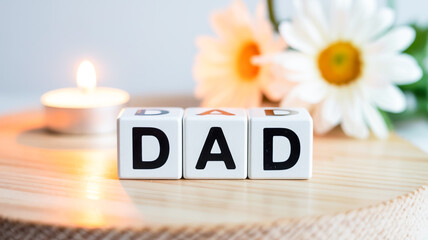 A close-up photograph of three white letter blocks spelling out DAD on a light wooden surface.