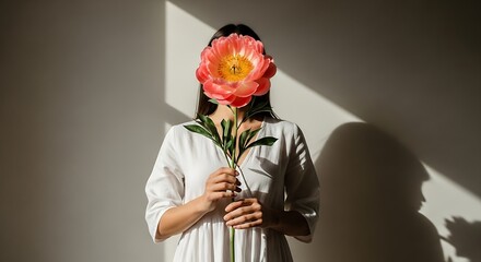 Woman holding large pink flower in front of face with light and shadow play