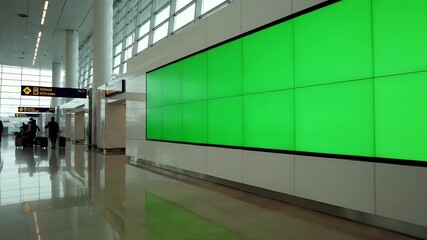 A large green screen video wall display for chroma key advertising mockups, situated in a modern, brightly lit airport terminal hall.
