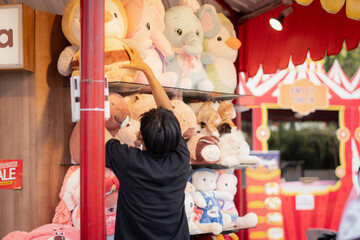 A male employee is tidying up dolls on an open shelf at a carnival