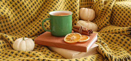 Plaid, books, cup of hot green tea and pumpkins on sofa in room