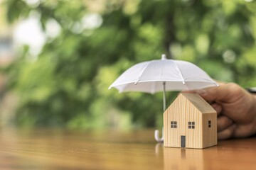 Wooden miniature house under white umbrella, home insurance protection safety concept.