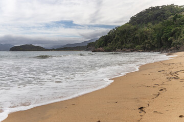 Ubatuba beach in São Paulo, with trees at the background, sand and waves.
Incredible paradisiac beach with cloudy sky.
