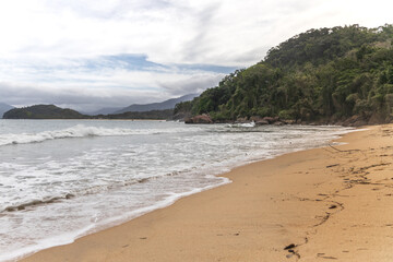Ubatuba beach in São Paulo, with trees at the background, sand and waves.
Incredible paradisiac beach with cloudy sky.