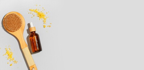 Bottle of essential oil, massage brush and sea salt on grey background with space for text