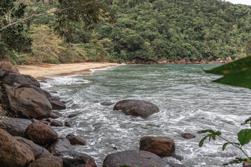 Ubatuba beach in São Paulo, with trees at the background, sand and waves.
Incredible paradisiac beach with cloudy sky.