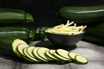 Many fresh zucchini and bowl with slices on grey tile table