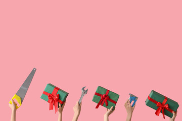 Hands holding construction tools and Christmas gifts on pink background