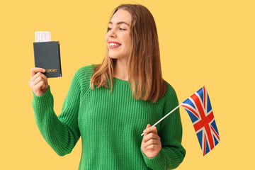 Beautiful young happy woman with UK flag, passport and ticket on yellow background