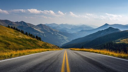 Fototapeta premium Mountain highway vista. Vast asphalt road stretches into a valley nestled amidst hazy blue mountains. Golden grasses and pine trees line the hillside. A clear, cloud-filled sky completes the scene