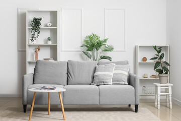 Interior of light living room with sofa, table and shelf units