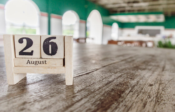 Wooden cube calendar for 26th August place on a table in a blur cafe background